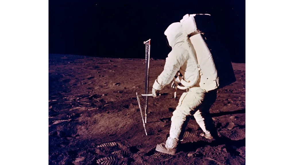 Astronauta in tuta spaziale bianca maneggia uno strumento scientifico sulla superficie grigia della Luna, con lo spazio nero sullo sfondo.