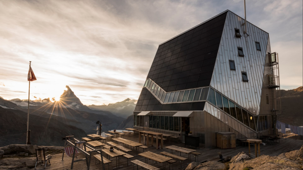 Edificio moderno in metallo con pannelli solari e terrazza in legno situato in montagna all’alba.
