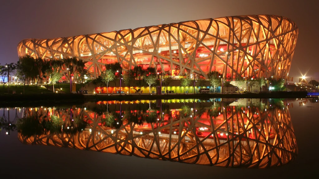 Vista notturna dello Stadio Nazionale di Pechino, detto Nido d'Uccello, con luci colorate e riflesso sull'acqua, situato nell’Olympic Green in Cina.