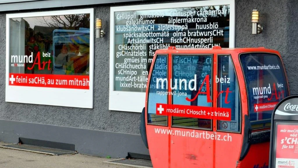 Painel publicitário de um restaurante escrito em suíço alemão.