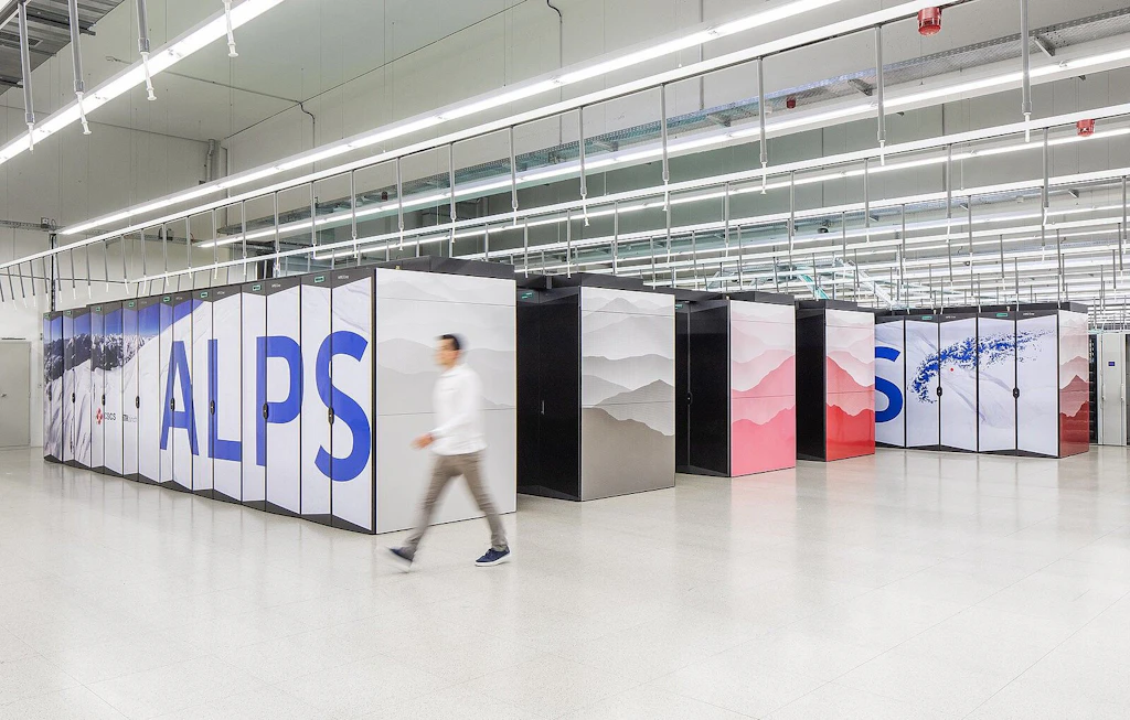 Больши электрошкафы для суперкомпьютера с маркировкой ALPS в ярко освещённом дата-центре; мимо проходит человек.